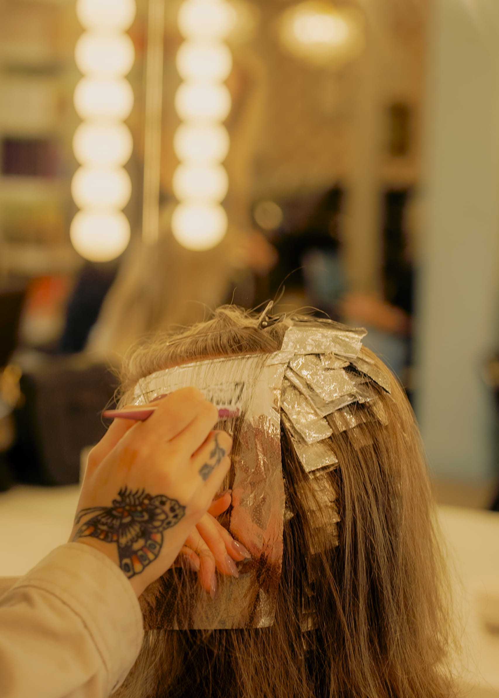 Hairdresser applying color to client's hair with foil wraps in a salon.