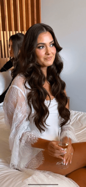 Woman in lace nightwear holding a glass of champagne, sitting on a bed.