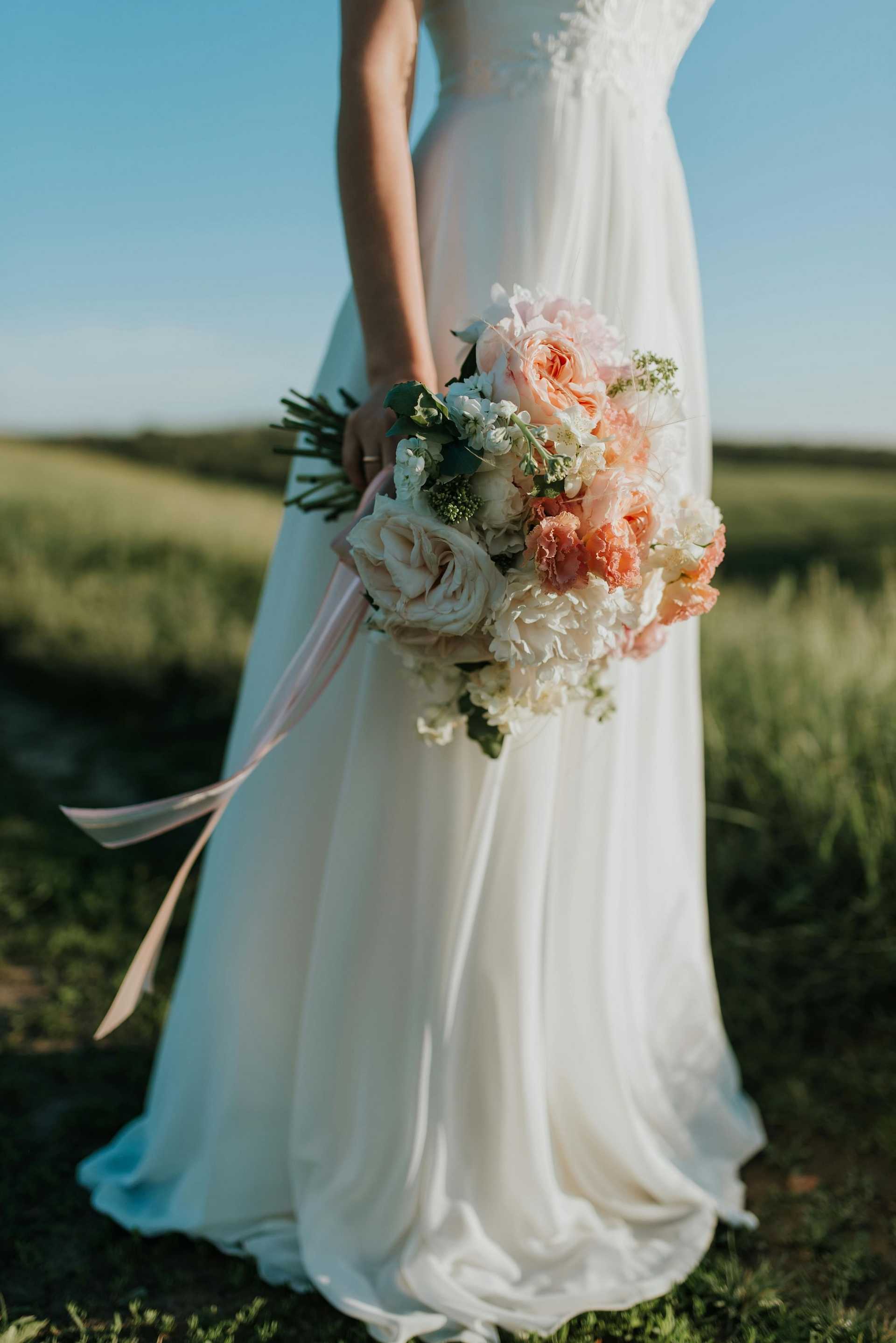 Bride holding a bouquet of pink and white flowers in a sunny field.