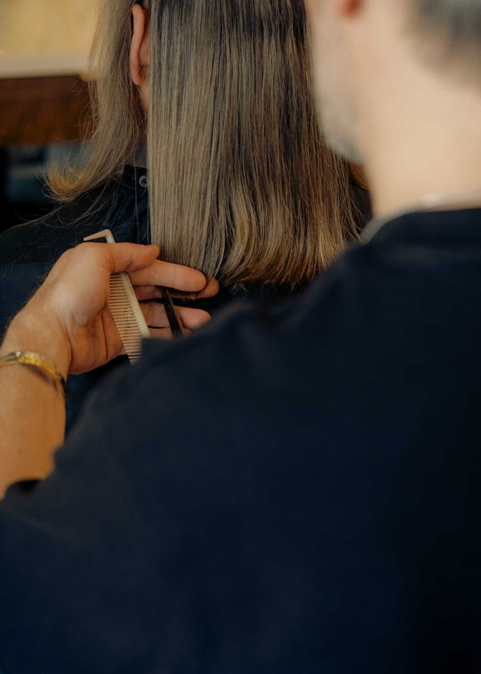 Person getting a haircut, with stylist trimming shoulder-length hair using scissors and comb.