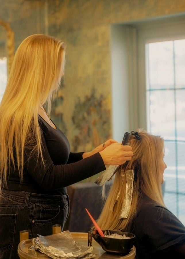 Hair stylist applying foil highlights to a woman's long hair in a salon setting.