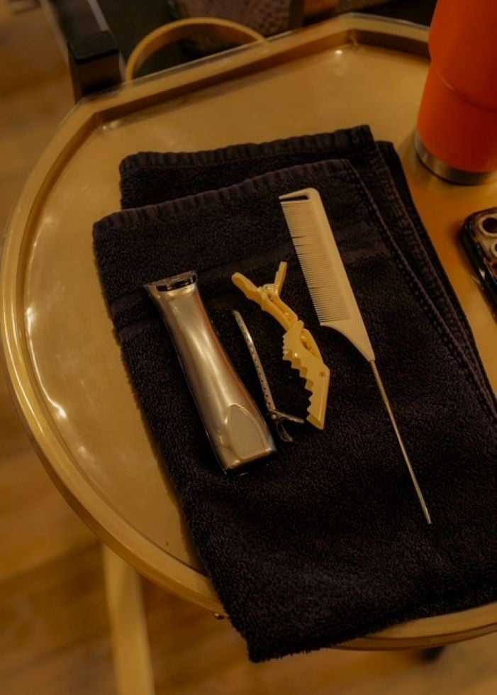 Grooming tools including trimmer, comb, and hair clip on a black towel on a tray.
