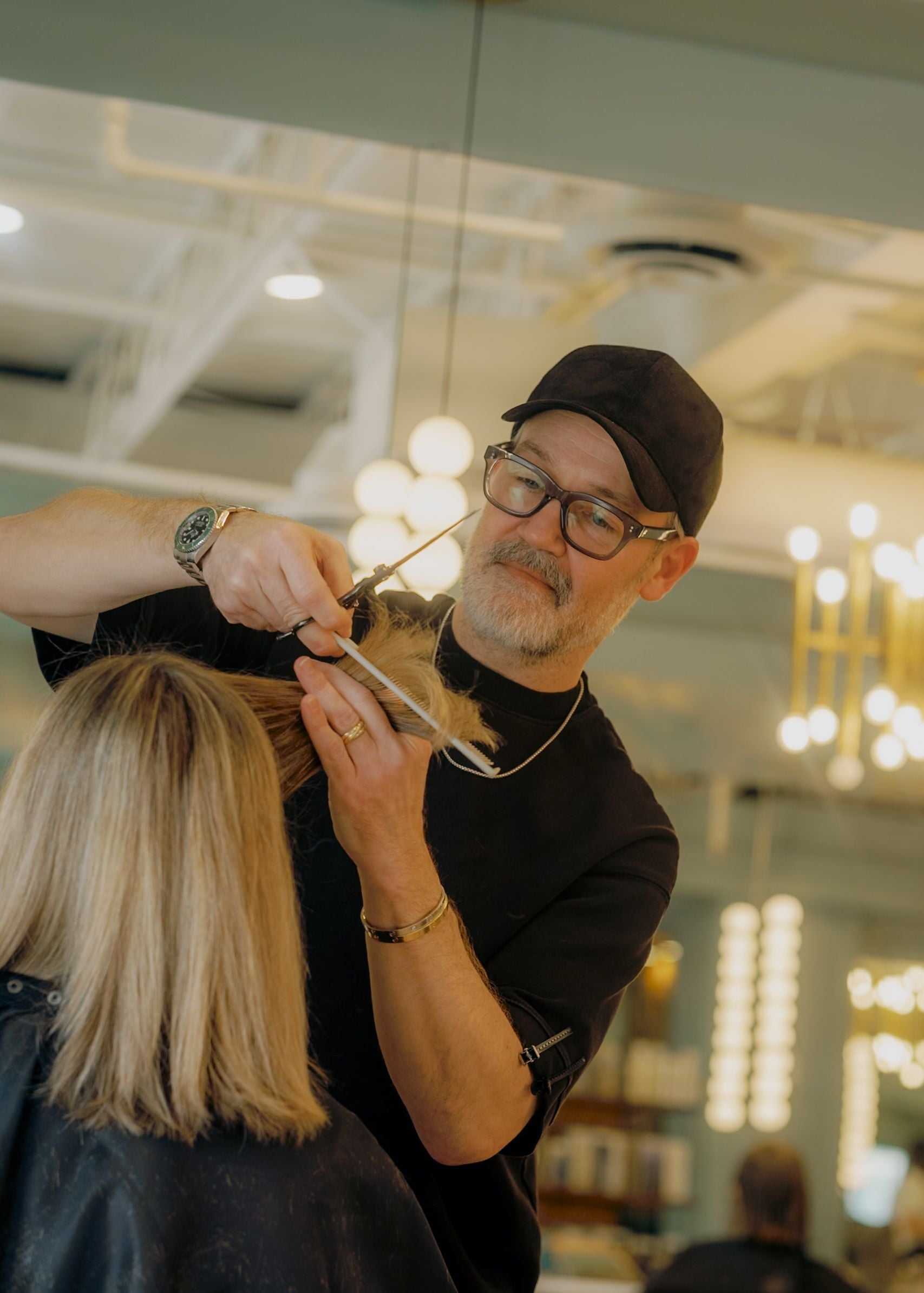 A hairstylist cuts a woman's blonde hair in a modern salon with bright lighting.