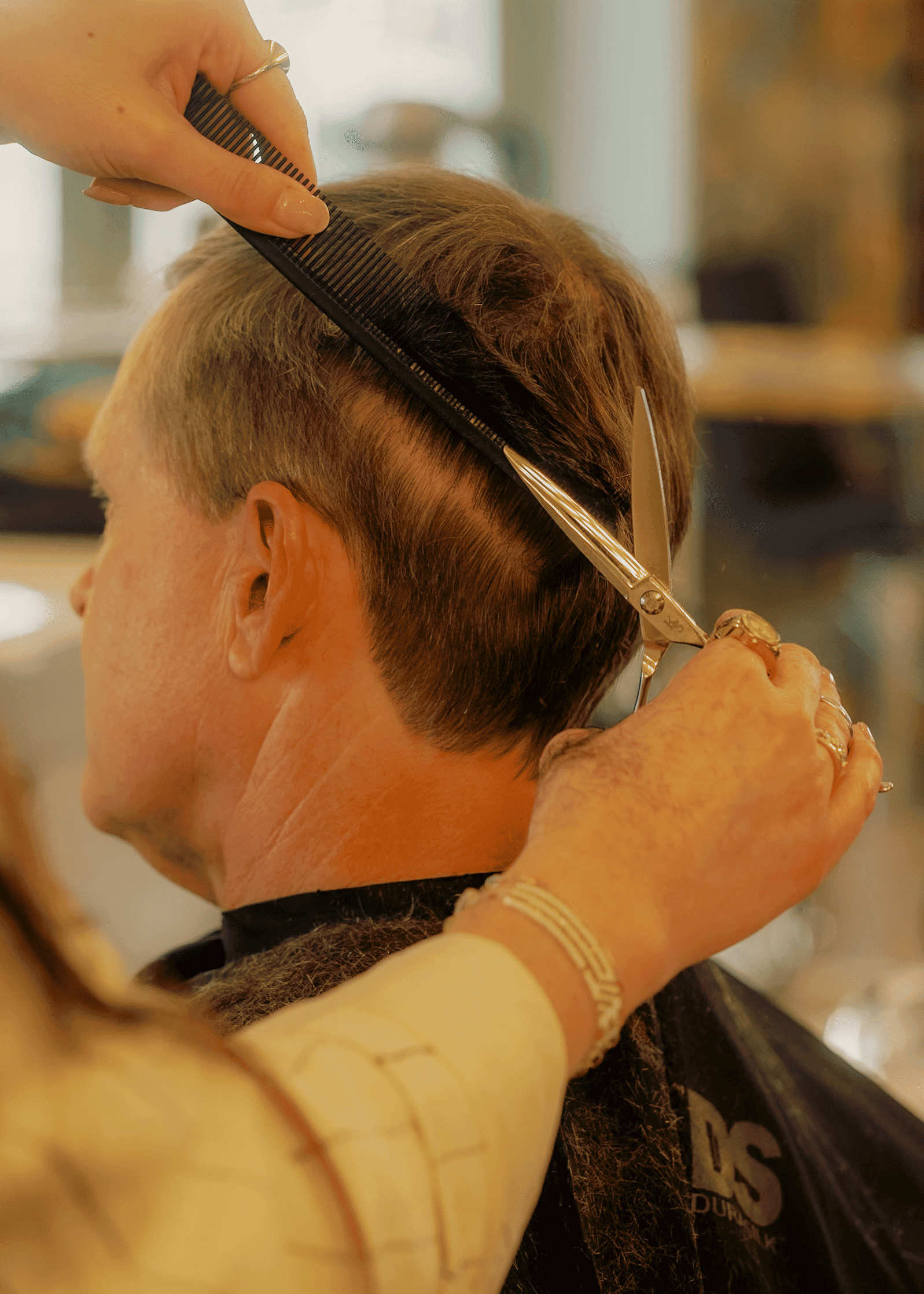 Person getting a haircut with scissors and comb in a salon. Hands of stylist in focus.